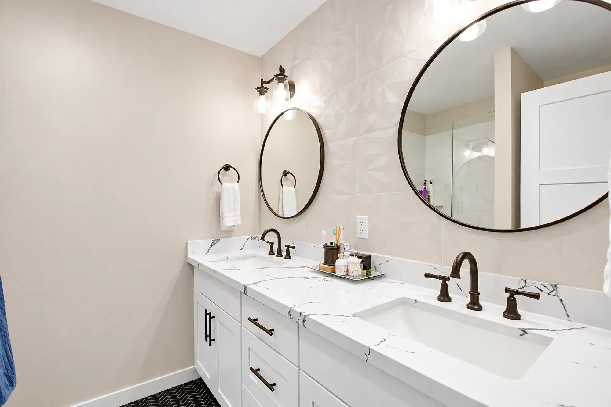 White double vanity with two round mirrors, dark faucets, and a textured tile backsplash.