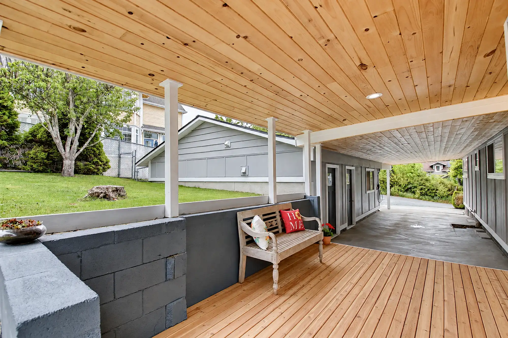Covered porch with a natural wood ceiling, matching decking, white posts, and a built-in bench.