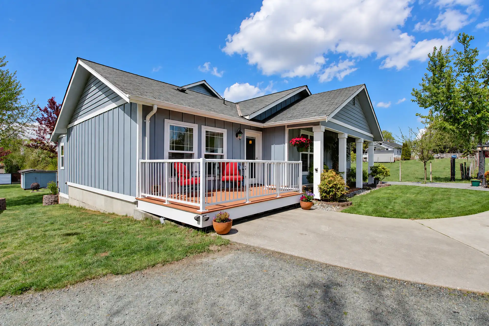 Gray home with white trim, a front deck, white railings, and a gabled covered entry, viewed from the side.