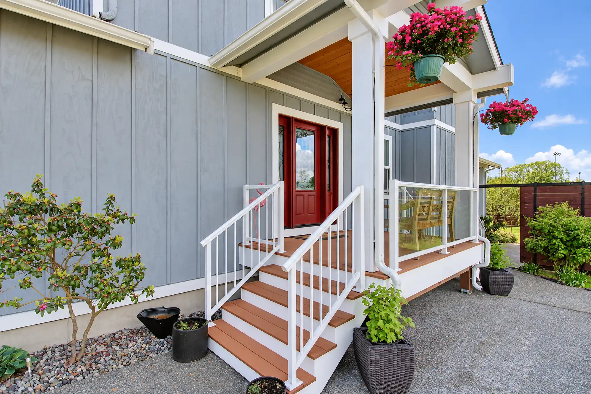 Covered entry with a red front door, wood-toned steps, white railings, gray siding, and hanging flower baskets.