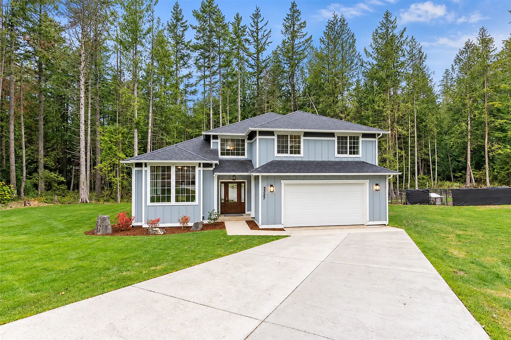 Gray two-story home with white trim, an attached two-car garage, a concrete driveway, and a wooded backdrop.