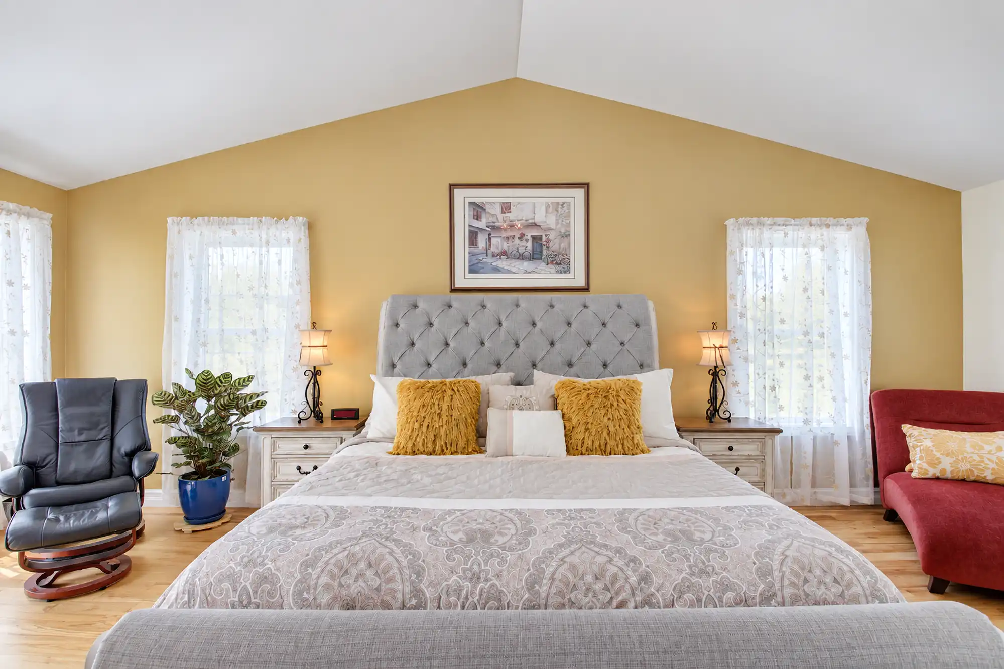 Front view of a tufted bed beneath a vaulted ceiling, with yellow walls, matching nightstands, and tall windows.