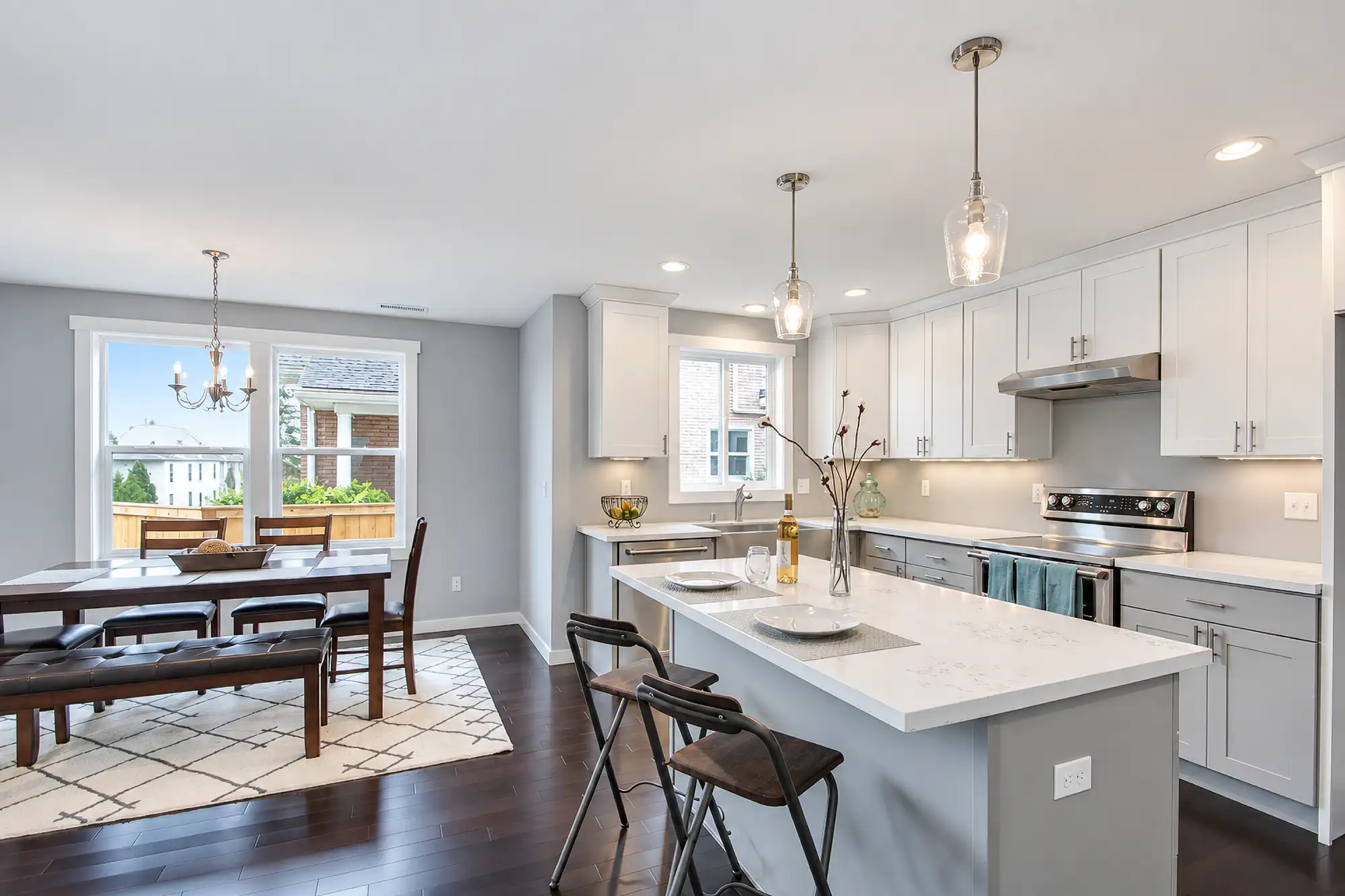 Kitchen island with two bar stools beside a window-lit dining nook, white cabinets, and stainless steel appliances.